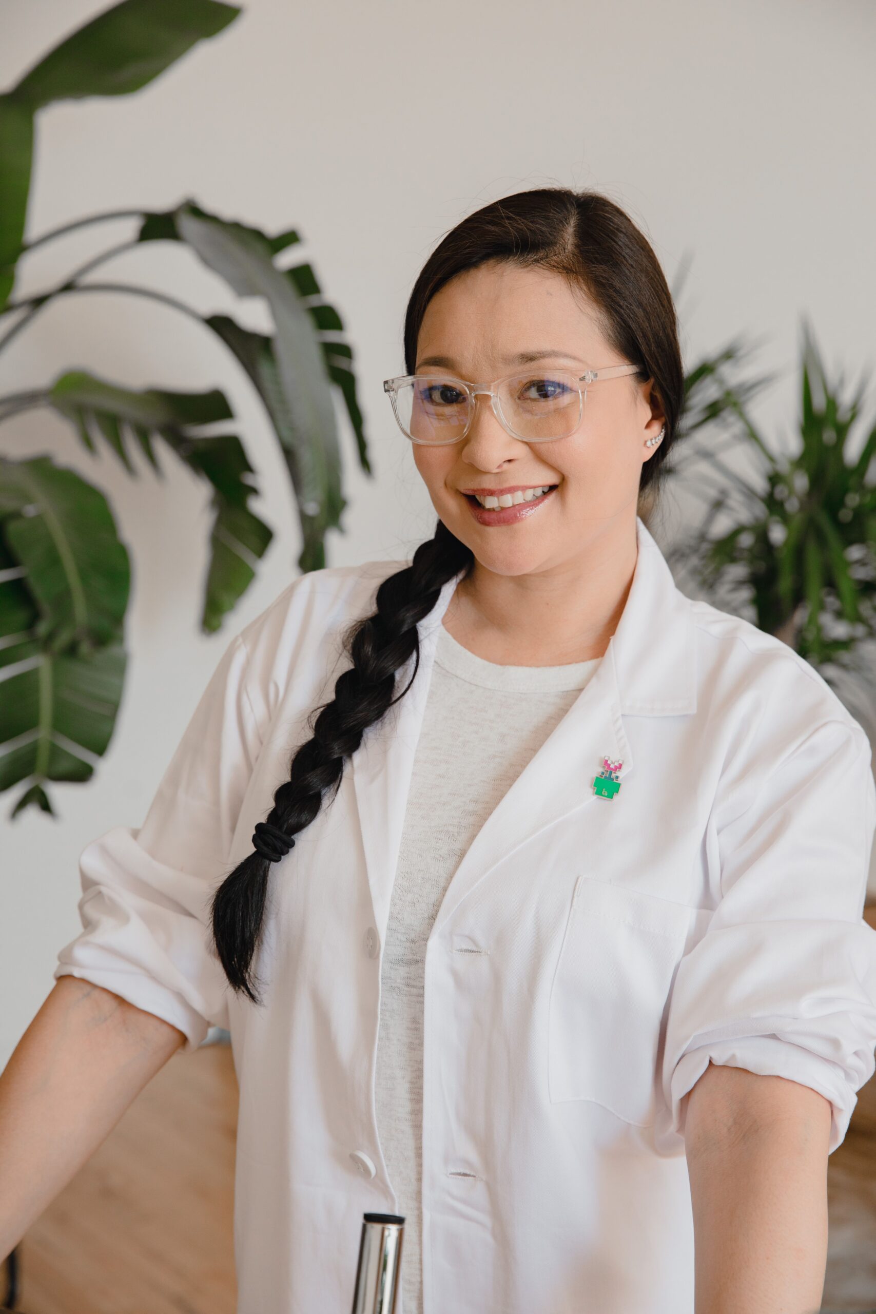 Pharmacist with braided hair smiling confidently in a lab coat, indoors.